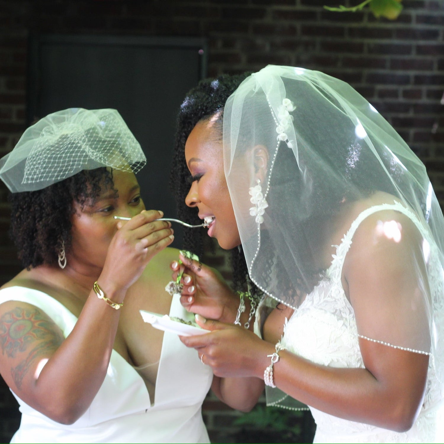 two brides feeding marble cake with strawberry buttercream wedding cake to each other on wedding day