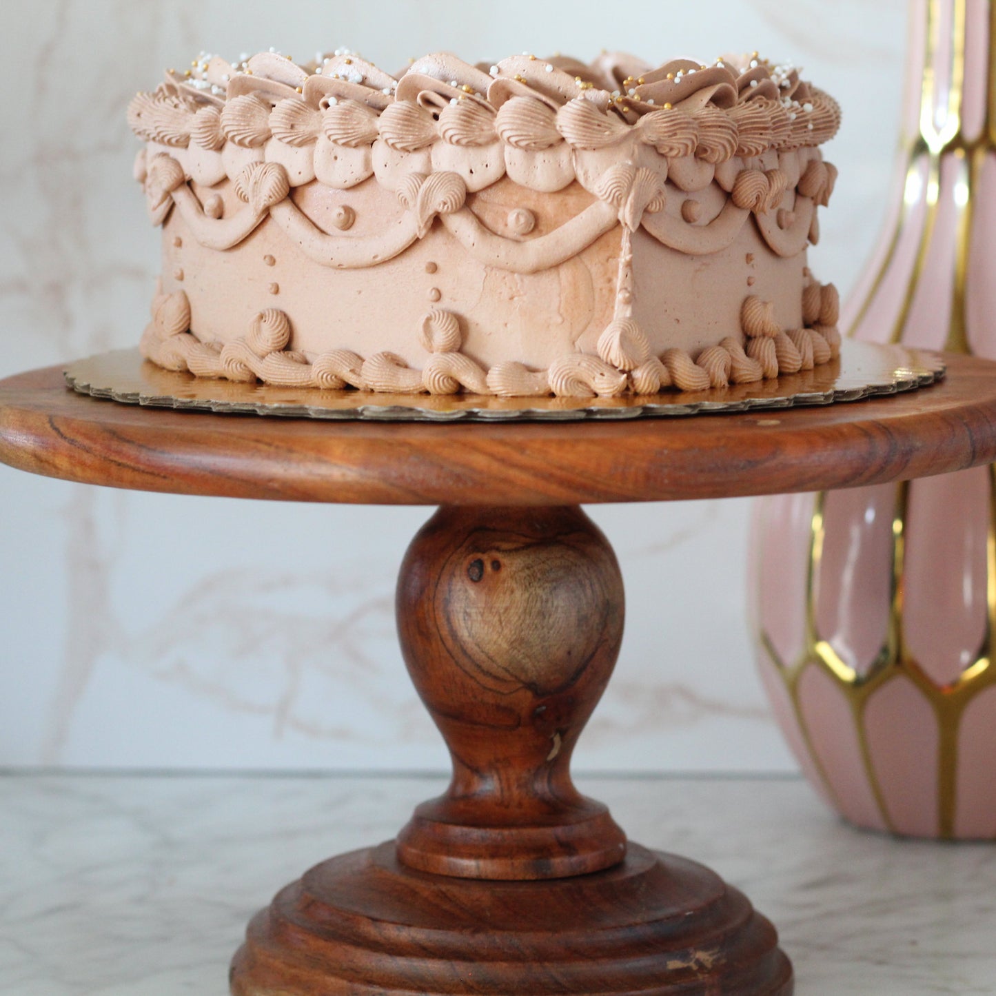Chocolate flavored Heart shaped cake on a wooden cake stand with a pink marble background