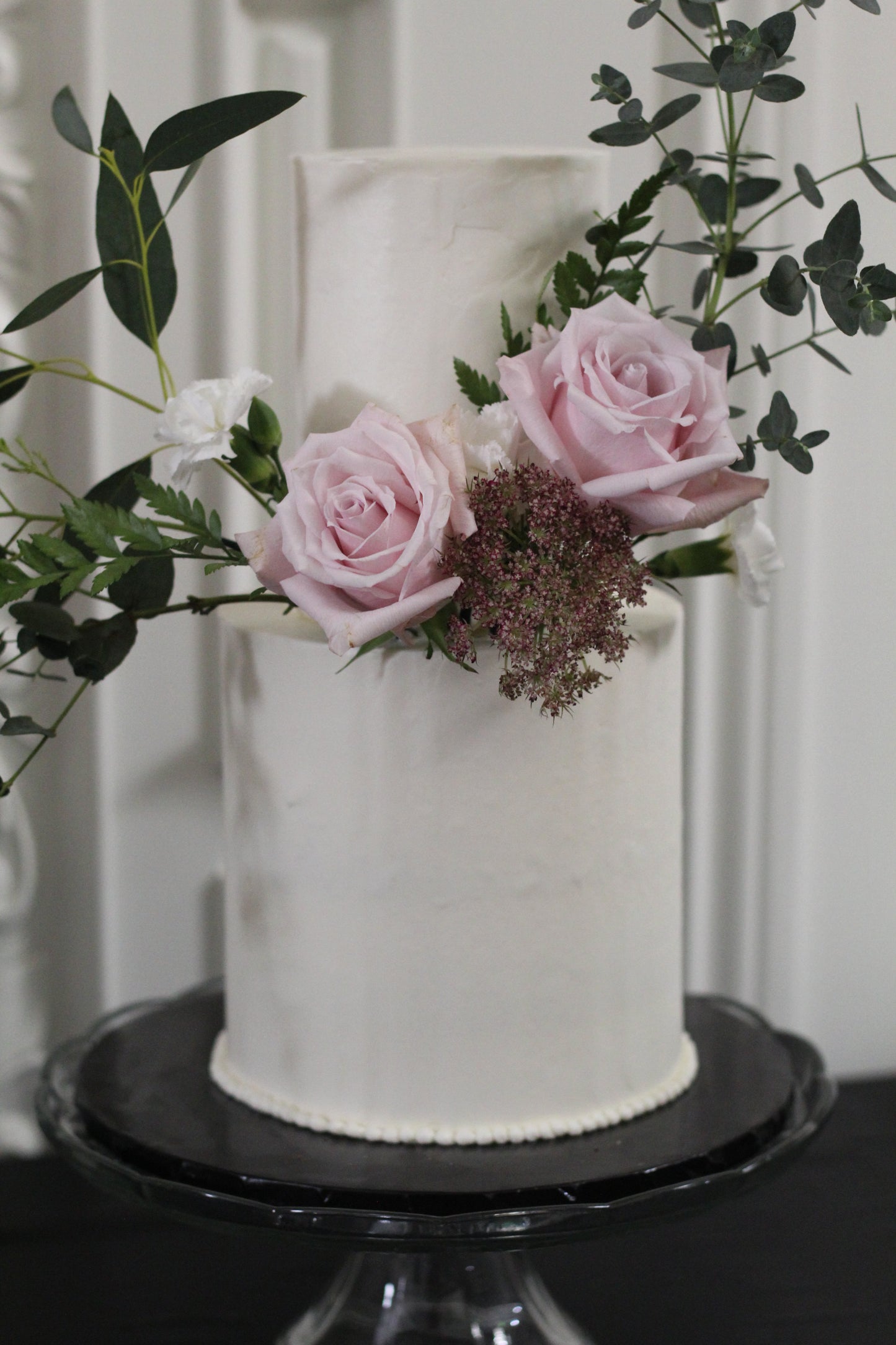 two tier white cake with pink roses and eucalyptus