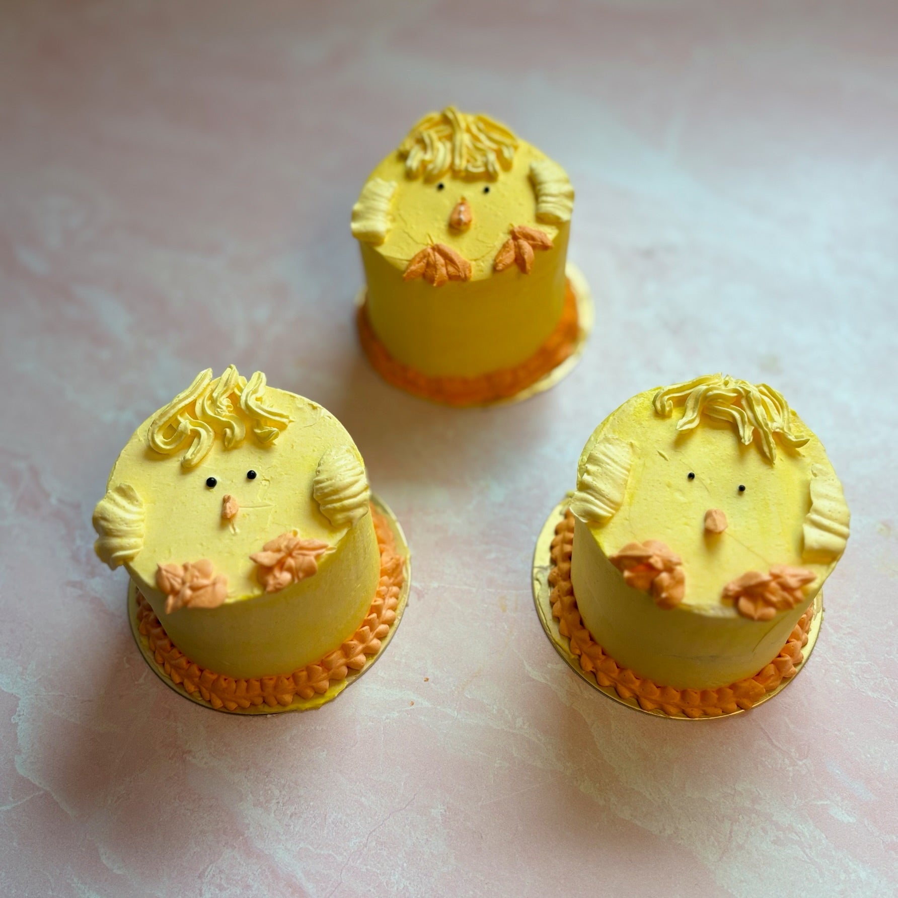 Three small yellow cakes shaped like chicks on a light pink background