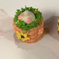 Small bunny butt sticking out of green grass, and pink and yellow flowers on a basket weave design
