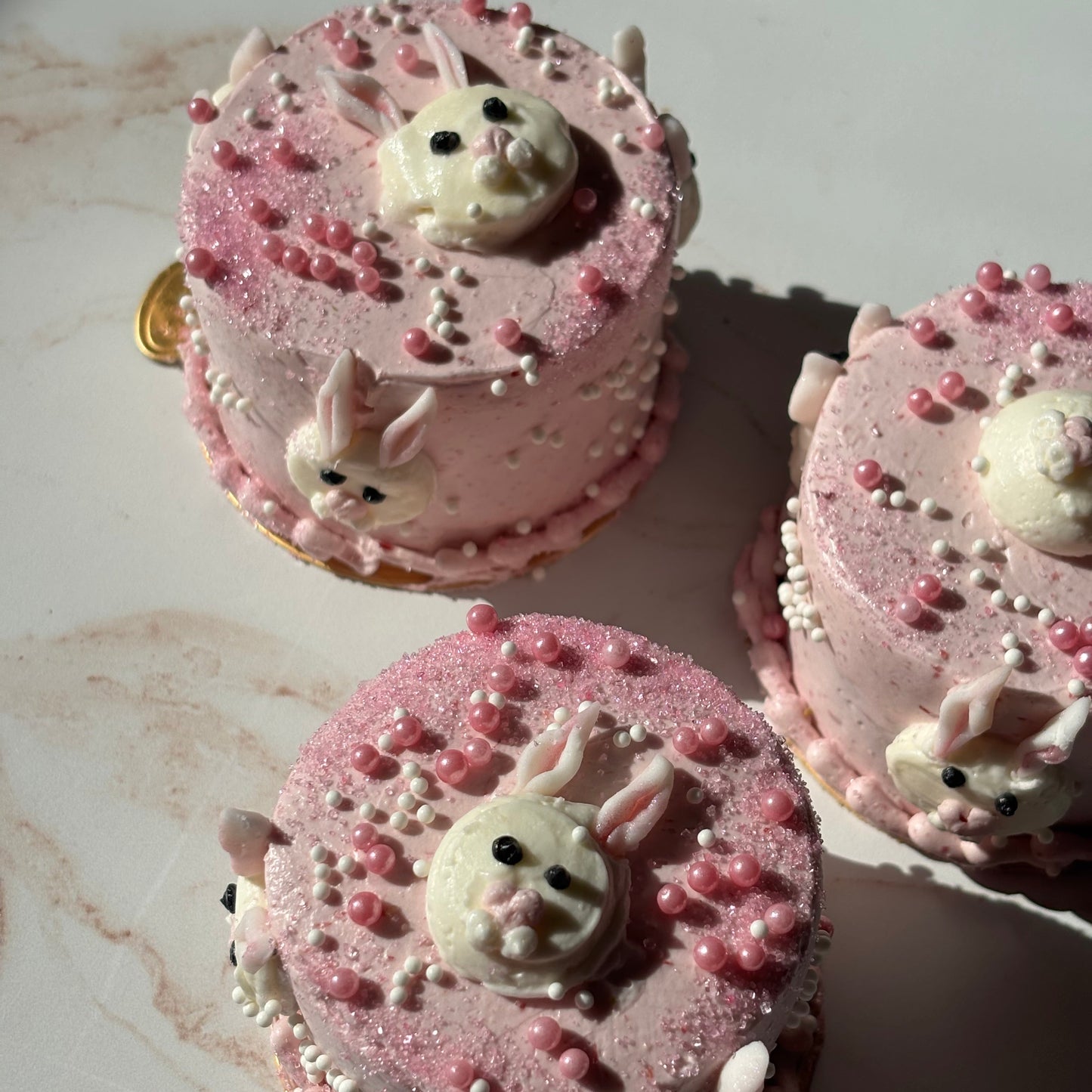 Pink cupcakes with bunny figures on a marble surface
